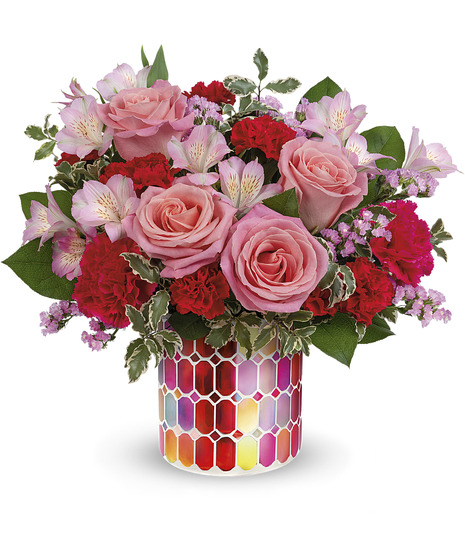 Bouquet of pink roses, red carnations, and assorted flowers arranged in a colorful, hexagon-patterned vase; green leaves surround the flowers, providing contrast.