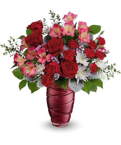 A red vase containing a bouquet of red and pale pink roses with green leaves and some gray foliage, placed against a plain white background.