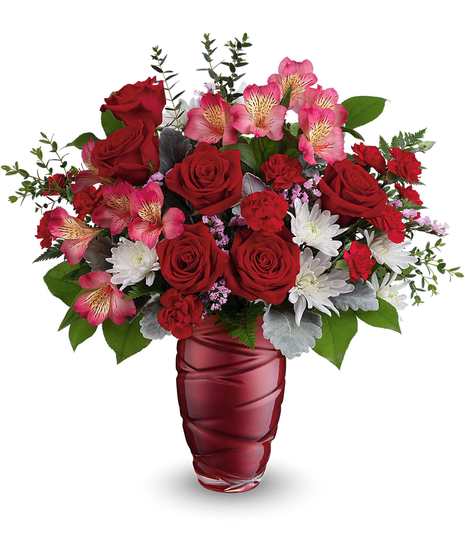 A red vase containing a bouquet of red and pale pink roses with green leaves and some gray foliage, placed against a plain white background.