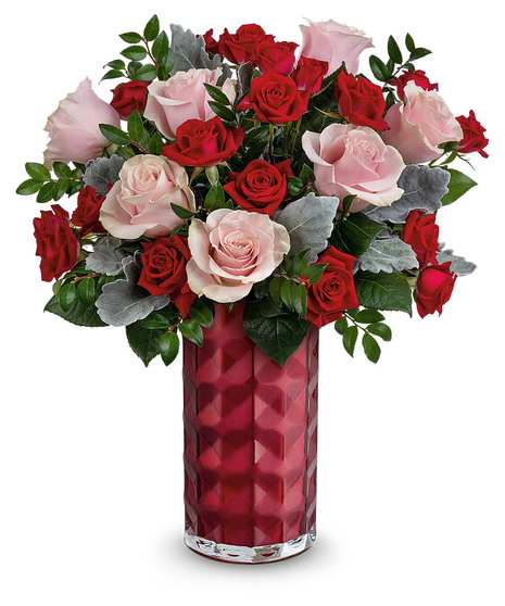 A red vase containing a bouquet of red and pale pink roses with green leaves and some gray foliage, placed against a plain white background.