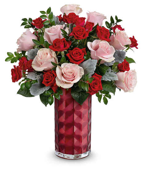 A red vase containing a bouquet of red and pale pink roses with green leaves and some gray foliage, placed against a plain white background.