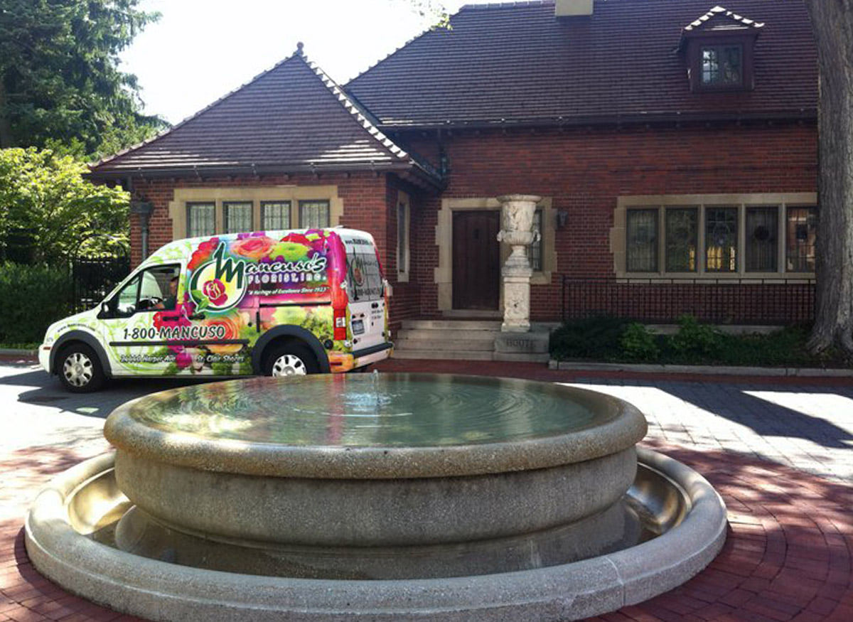 A Mancusos-branded van makes its delivery behind a babbling water fountain